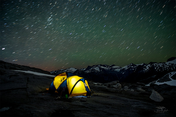 Starry night sky over yellow north face tent with mountains in the background. Photography by Shel Neufeld from Roberts Creek, BC, Canada.