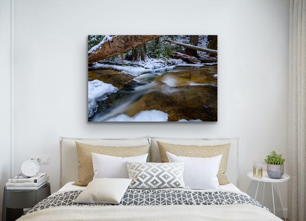 A large photography wall art hangs in a bedroom. The wall art contains icy water flowing over a rockbed in a winter forest. Photography by Shel Neufeld. 