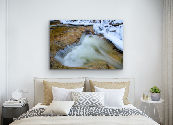 A rock and waterfall form a heart shape in nature. Captured by Shel Neufeld and available as a fine art photography print in a variety of sizes and mediums. The artwork hangs in a  bedroom. 