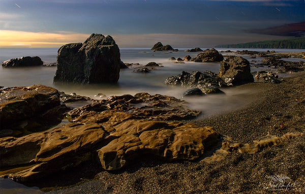 Dusk on a rocky shore is captured by landscape and nature photographer Shel Neufeld. Soft waves come to the shore. 