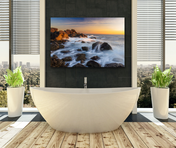 Ucluelet Waves Landscape Photography Canvas hangs in a bathroom scene above a large white soaker bathtub. The bathroom has large floor to ceiling windows and a city in the distance. The image is meant to help visualize what the coastal landscape canvas could look like in a bathroom setting. Artwork by Shel Neufeld, Canadian landscape and nature photographer. 