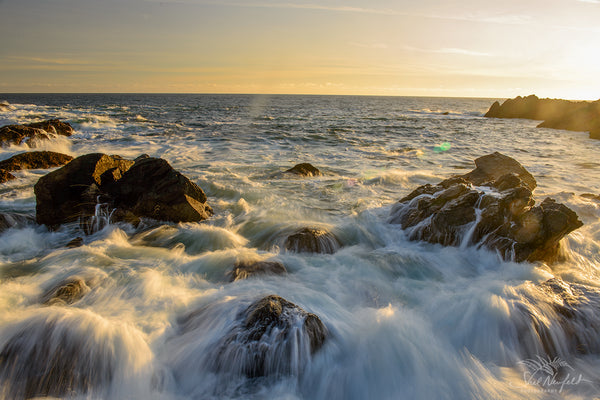 Ucluelet Water crashing beach landscape scene by Shel Neufeld. Blue and yellow tones fill the image as waves come crashing over the rocks on shore. 