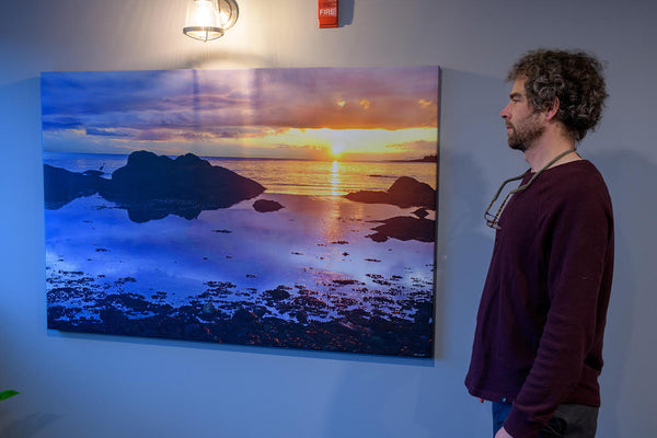 Artist Shel Neufeld stands in front of a photography canvas of his work. His photography is available to be printed in a variety of sizes on several mediums. 