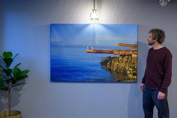 Photographer Shel Neufeld stands in front of one of his custom printed photography canvases. He is trying to show the scale of the canvas in relation to his body size. 