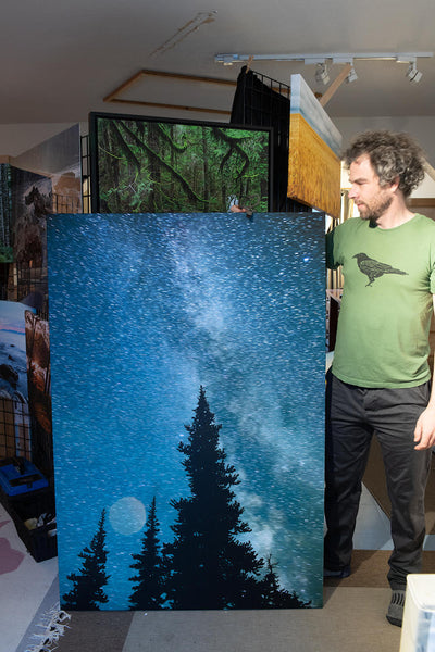 Canadian photographer, Shel Neufeld, stands beside a custom printed astrophotography image. 