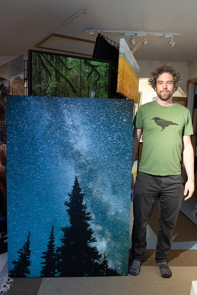 Canadian photographer, Shel Neufeld, stands beside a custom printed astrophotography image. 